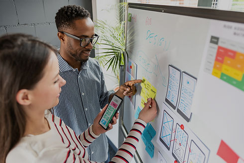 Two individuals working on a white board with sticky notes.