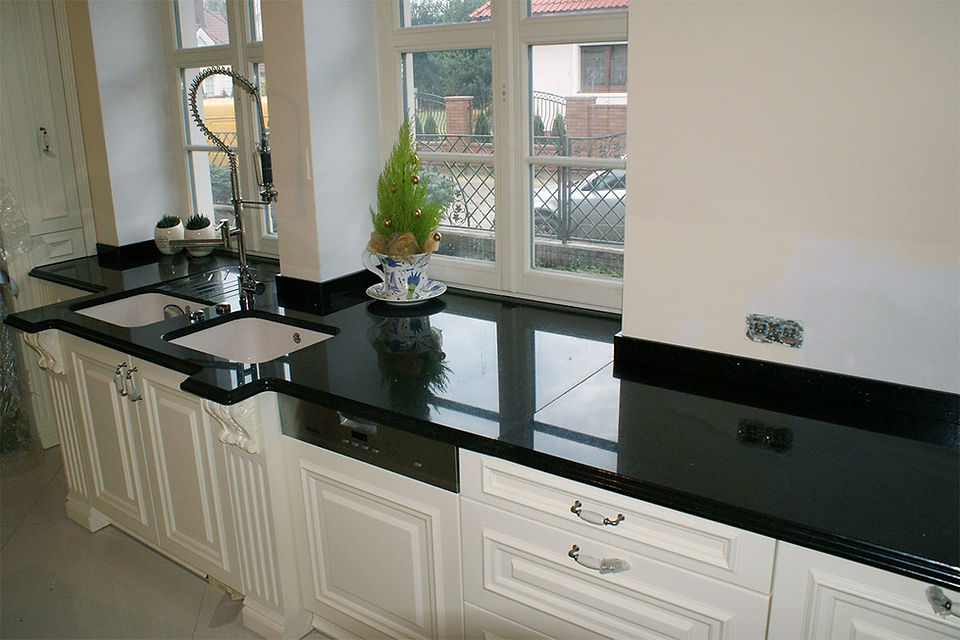Luxury kitchen interior featuring premium Black Granite countertops and full-height backsplash from Aravali Marbles, showcasing bold natural veining, high-gloss finish, and a modern brass faucet installation.