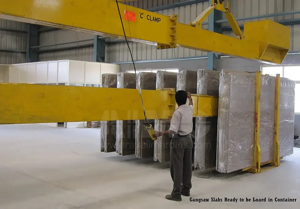 Worker operating a crane with C-clamp to lift securely packed gangsaw granite slabs for container loading at Aravali India Marbles & Granites warehouse.