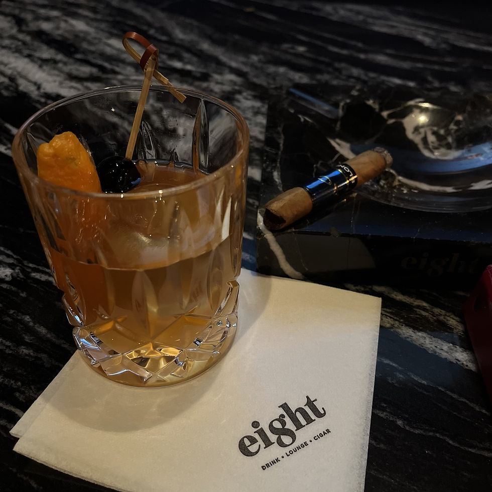 Old fashioned cocktail with orange peel and cherry beside a cigar on a marble bar at a Las Vegas cigar lounge, illustrating whiskey and cigar travel experiences.