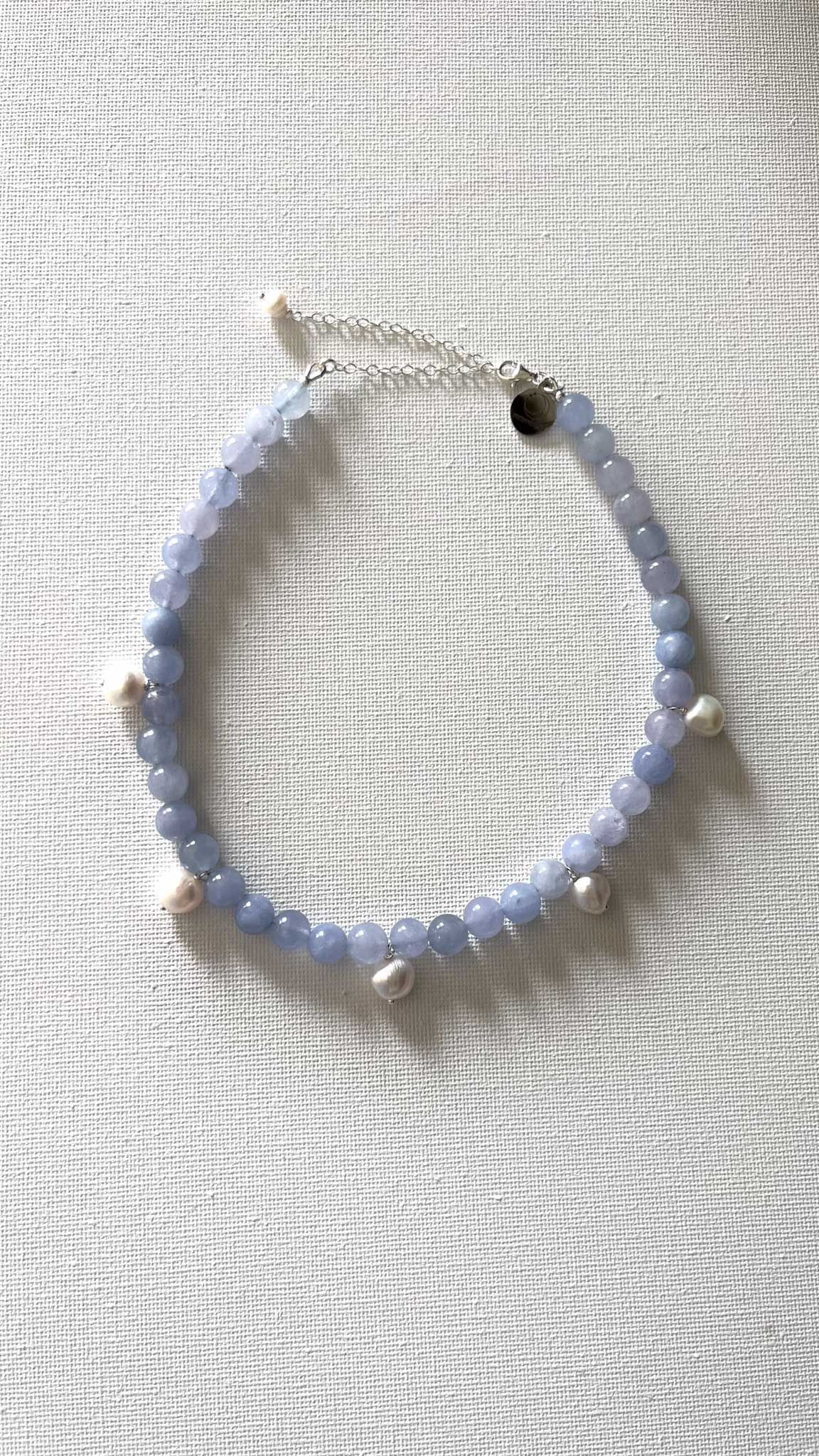 שרשרת ציפור עשויה מאבנים ג׳ייד עגולות בגודל 8 צ״מ בצבע תכלת בשילוב 5 פנינים בגודל בינוני.