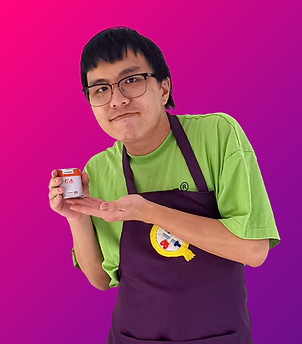 A half-body portrait of D, a young Chinese male in his 20's. He is clean-shaven and wears glasses. He's wearing a green t-shirt underneath the Qiqi's Cosplay Medics purple apron. He is posing with both hands displaying a can of contact adhesive.