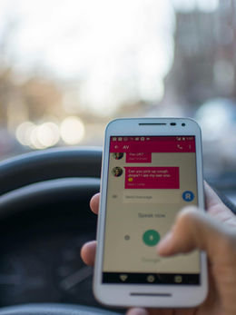 Person texting while driving with their phone in their right hand held up right in front of the wheel.