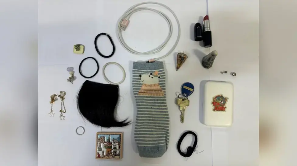 Assorted items on a table: sock, earrings, lipstick, hair ties, cable, key, Tom and Jerry case, all on white background. Collected as trophies by serial rapist Zhenhao Zou. London crime.