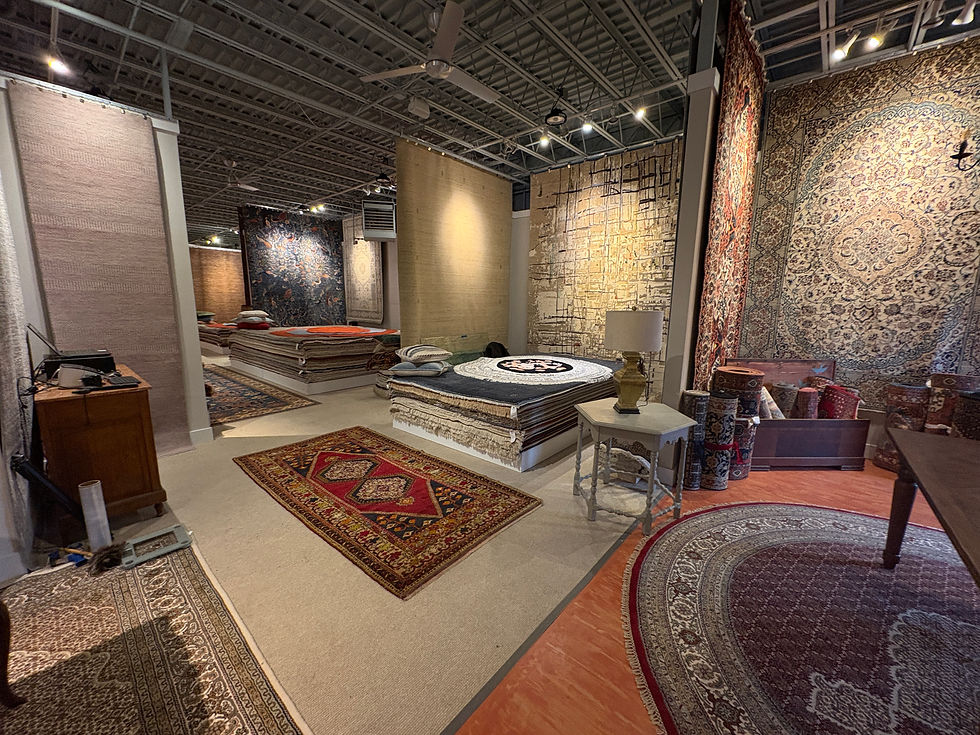 Rug showroom with hanging Persian carpets, stacked rugs, lamps, and patterned floor rugs under bright industrial lighting