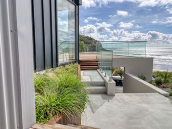 Concrete patio leading to wooden decking with glass balustrade 