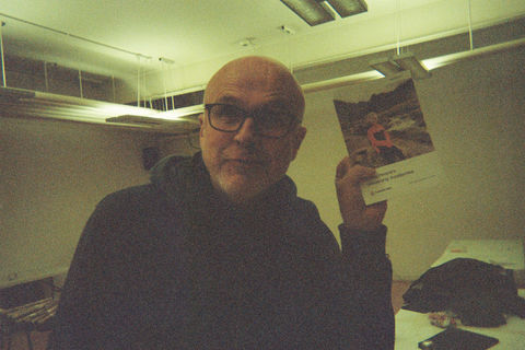 Tim pouts towards the camera, holding up a flyer.