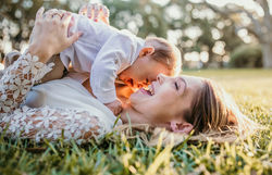 Sunset in nature with a mother and her baby boy laying on the grass laughing