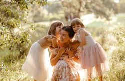 Sunset photo of mum being hugged by her twin girls in nature