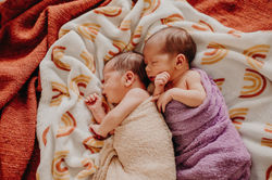 Newborn twins sleeping next to each other on the bed