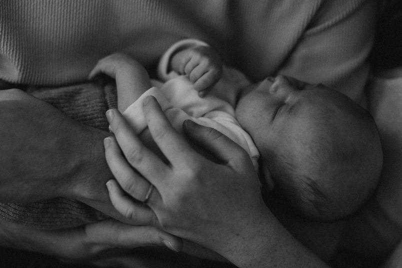 Ein Neugeborenes liegt liebevoll in den Armen der Eltern.