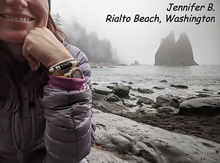 Photo of a customer wearing an Islands To Highlands Bracelet with the misty, rocky coast of Washington in the background. She is wearing a Tiki-themed bracelet.