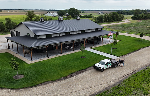 Aerial view of a custom Beachy Barndominiums home with wraparound covered porch and attached garage