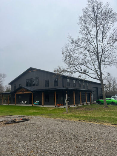 Dark gray custom barndominium with covered porch in a wooded setting