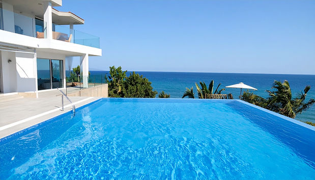 Stunning infinity pool overlooking the ocean from a modern white villa. Palm trees, clear
