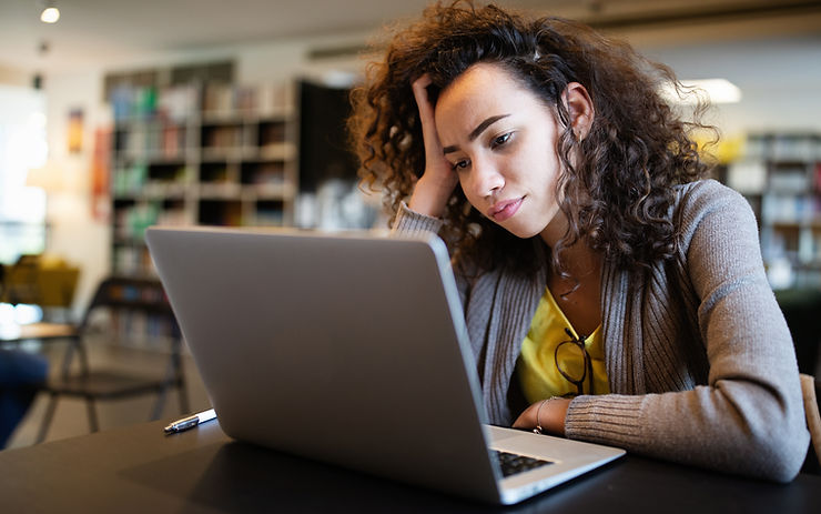 A young woman at the library deep in thought in front of her laptop