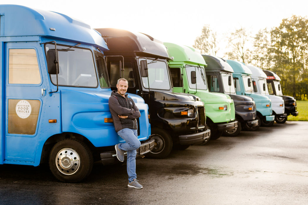 Mann lehnt an blauem SWEET HOME Food Truck, viele bunte LKWs.