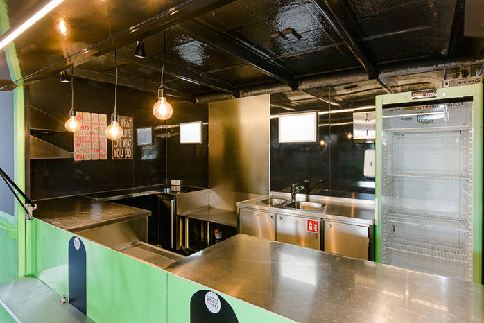 Moderne Küche mit Edelstahltheke, Hängelampen, schwarzen Decken und grünen Paneelen.