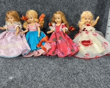 Four vintage dolls in colorful dresses lined up for auction