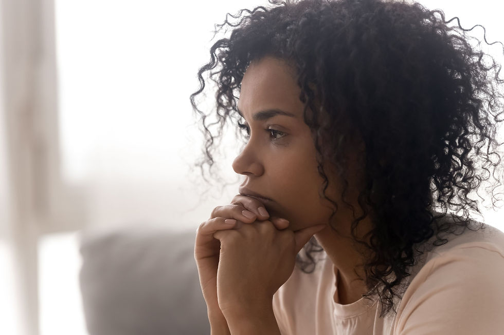 Thoughtful woman in profile rests her chin on clasped hands by a bright window, gazing downward in quiet reflection
