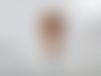 Woman in glasses covers face with hands, seated at a white desk with a laptop, lamp, and crumpled papers. Mood: stressed.