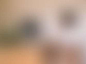 Person in white shirt video calls another on a desktop in a warm-lit room with a wooden desk and a plant, both appear engaged and smiling.