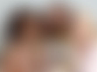 Three women laughing and holding blue mugs, wearing pearls and pastel sweaters, against a plain background. They appear joyful and relaxed.