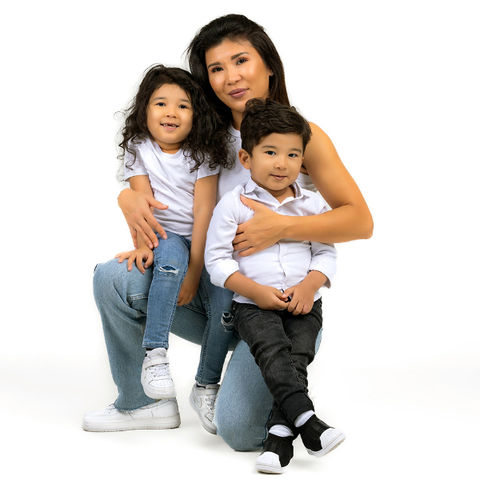 A mother seated with one knee on the ground, holding her son and daughter on each side, radiating love and connection.