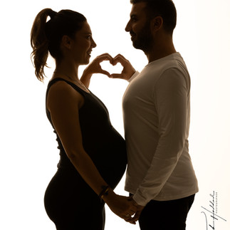A silhouetted couple stands face-to-face, forming a heart shape with their hands over the woman's baby bump.