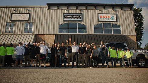armored roofing and construction team waving to camera in front of office