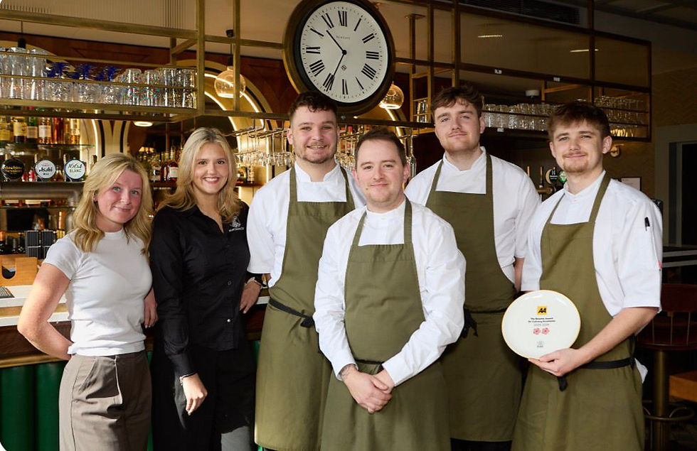 The Machine Inn team stand smiling in a bar setting, with a large clock above. One holds the 2AA award. Warm, welcoming vibe.