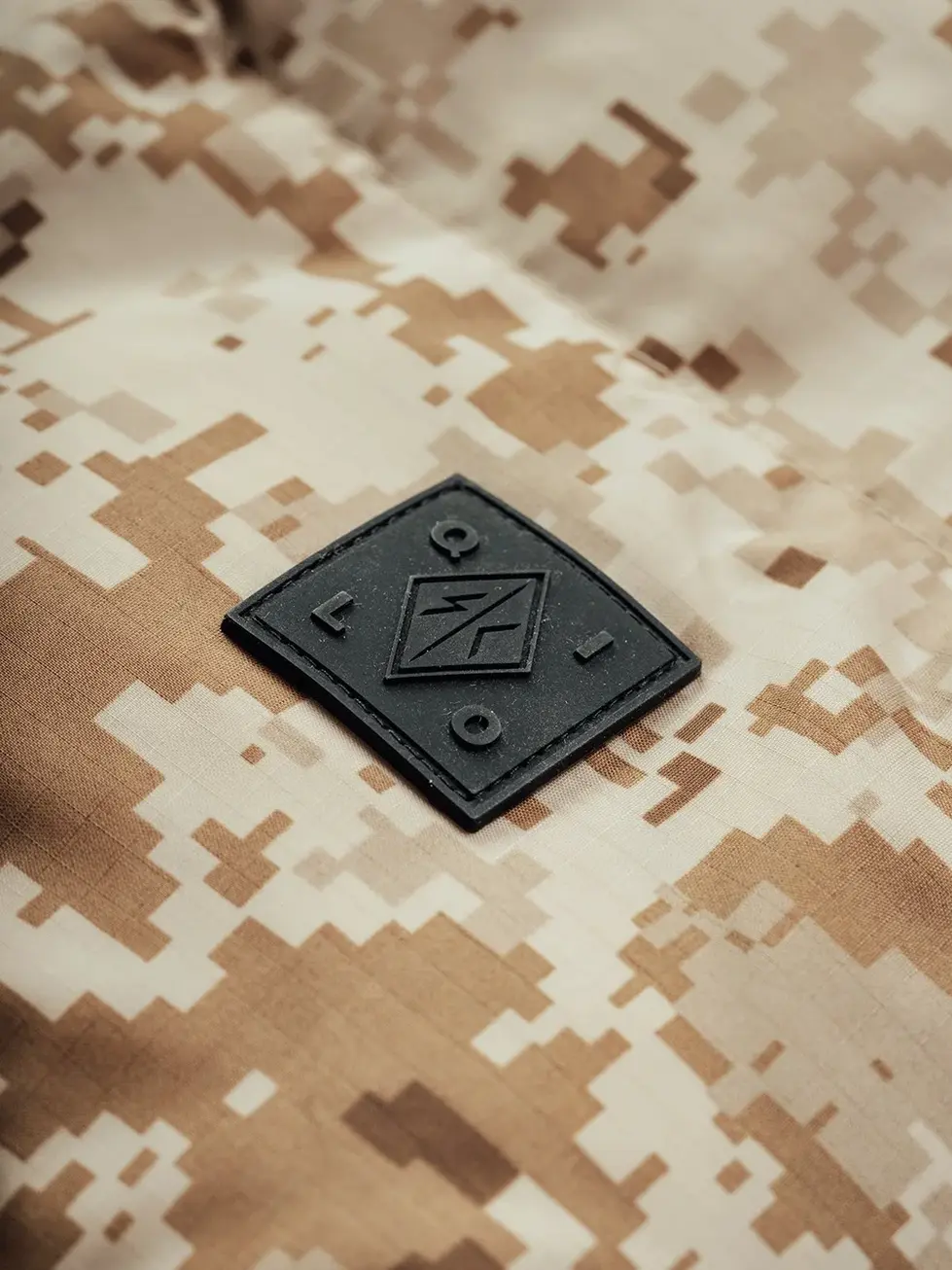 Details of a black embossed QILO x SC Irregulars logo on AOR1 LHTOSE down puffer jacket