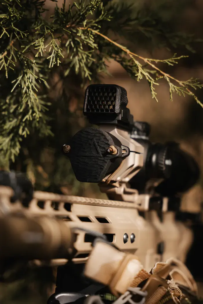 A tan AR15 rifle with an LPVO, which has a One Hundred Concepts ScopeCap Pro™ Ruggedized attached to the front lens