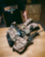 AOR1-pattern plate carrier equipped with Ferro Concepts pouches, mag inserts, radio pouch, and antenna, displayed on wooden surface by operator in black Noveske T-shirt.