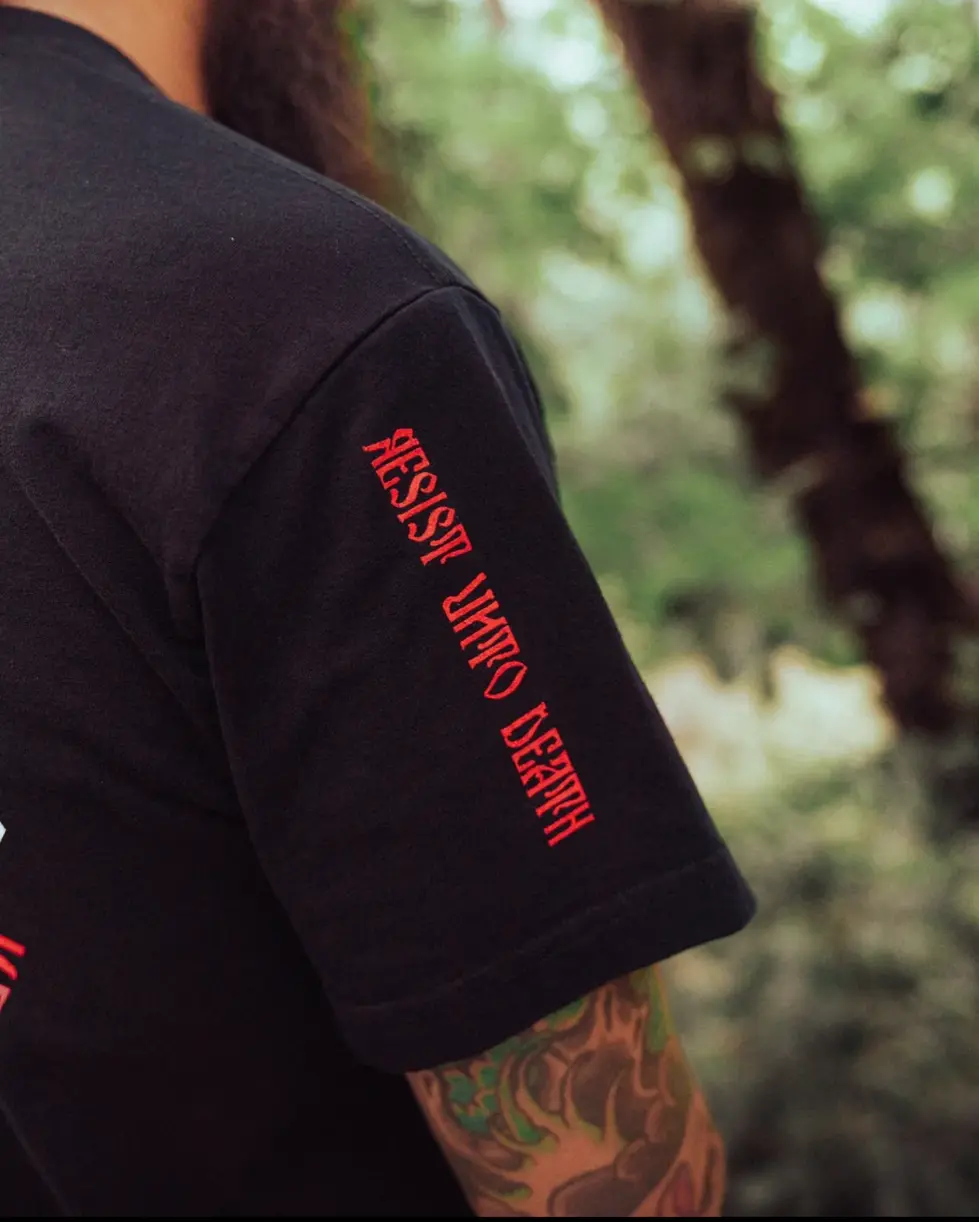 Detailed close up of the "RESIST UNTO DEATH" wording in red on the sleeve of a black SC Irregulars JESUS PRAYER S/S shirt