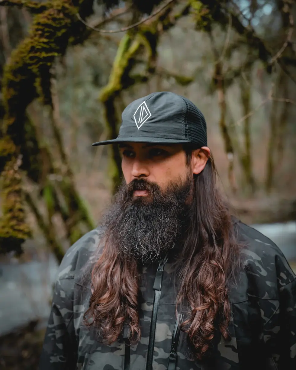 A person wearing SC Irregulars ID Mesh Back Pack Hat in a forest setting