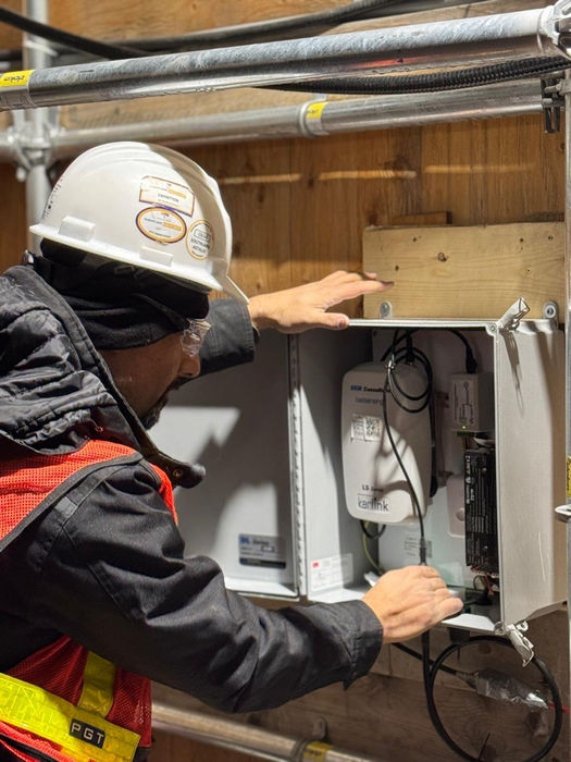 PGT technician inspecting and adjusting equipment inside a monitoring enclosure at a construction site.