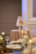 A white wedding cake in the distance adorned by beige and yellow florals
