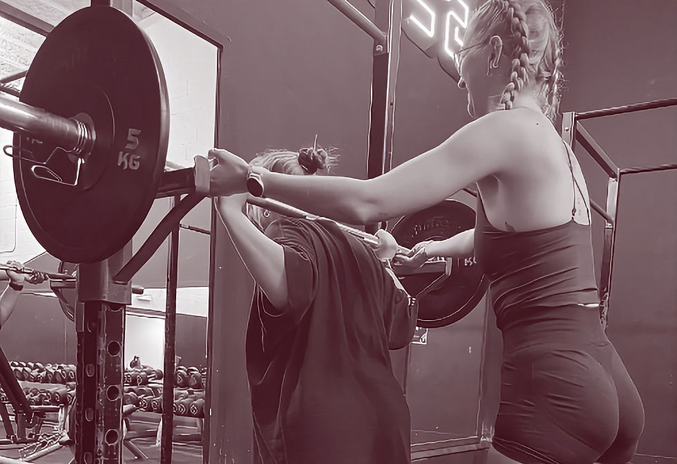 A personal trainer supporting a client in doing a back squat