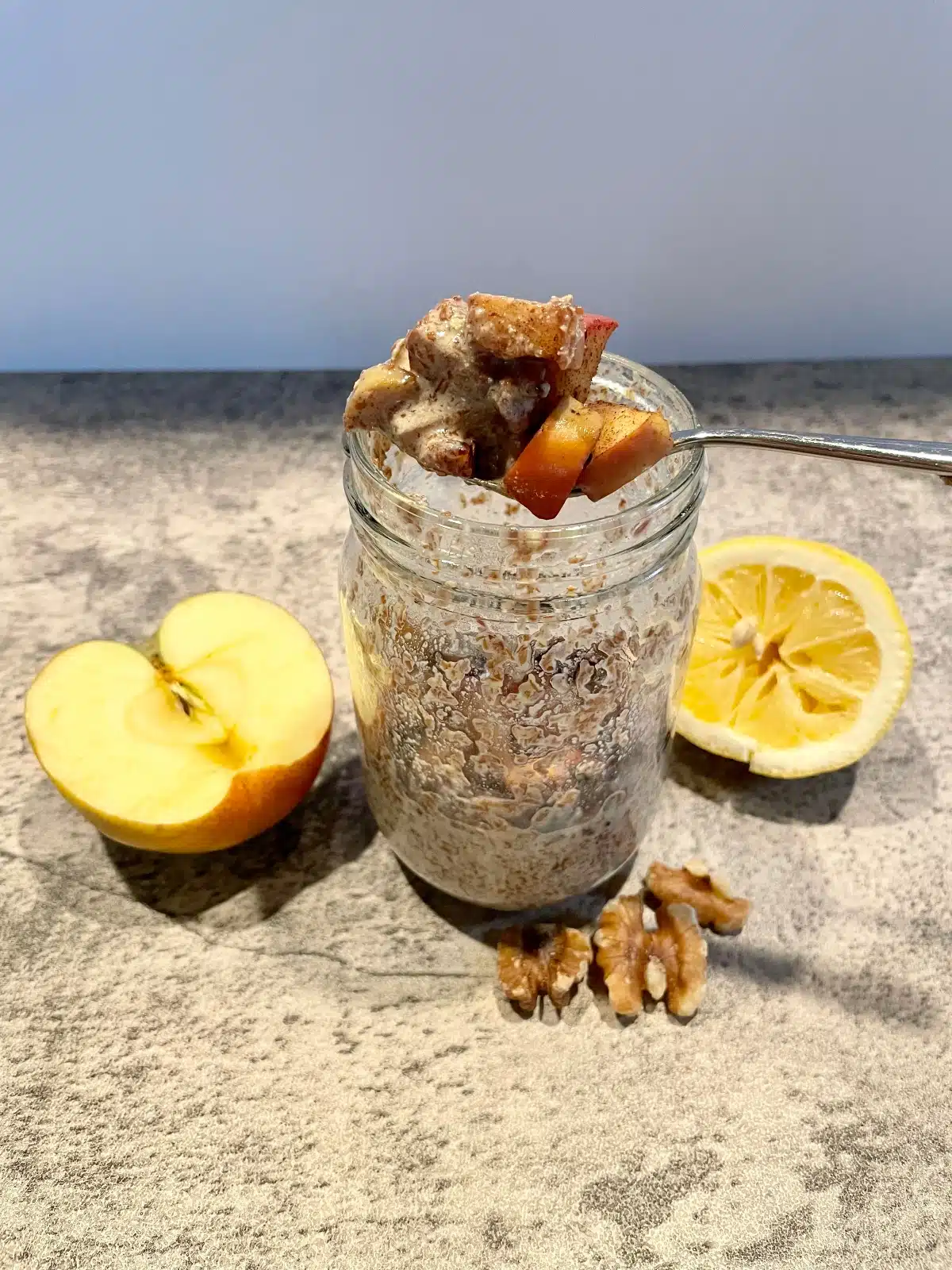 Image of a mason jar filled with chia pudding with apples and walnuts on top and sliced apple, lemon, and walnut halves on the side.