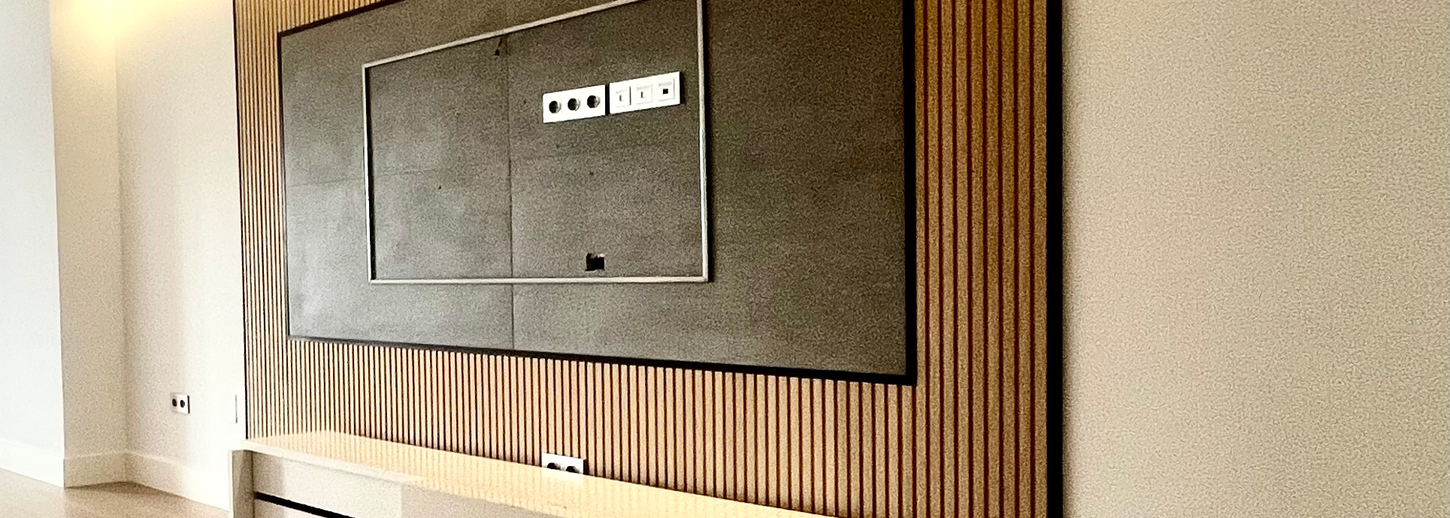 Salón principal con mueble bajo para televisión de diseño flotante y panel decorativo gris al fondo en Cánovas del Castillo, Malagueta.