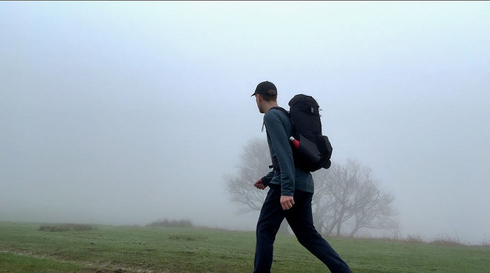 Man walking with backpack on, fog covered landscape and a singular tree.