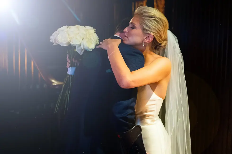 Bride embracing a man in a dark suit while holding a white bouquet.