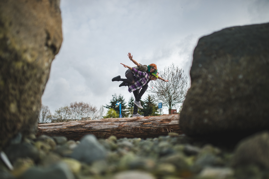 Two people in midair above a log, framed between large foreground rocks.