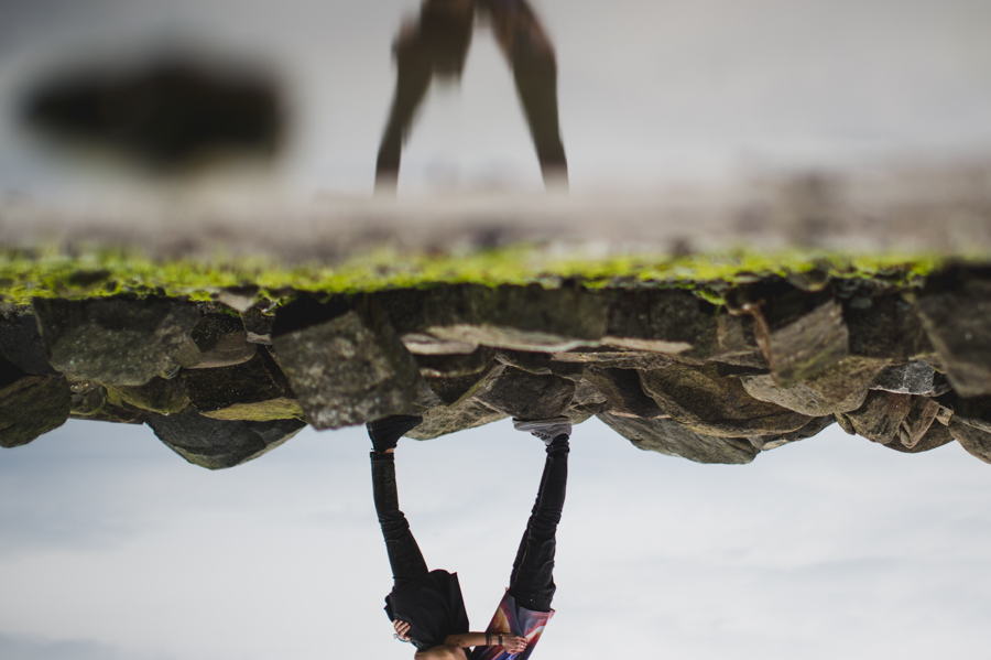 An inverted view of rocks and a person’s legs beside the shore.