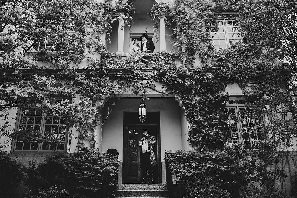 People framed by an upper window and a doorway of an ivy-covered white building