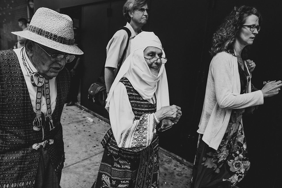 Black-and-white photograph of people in patterned clothing and head coverings walking through a doorway.