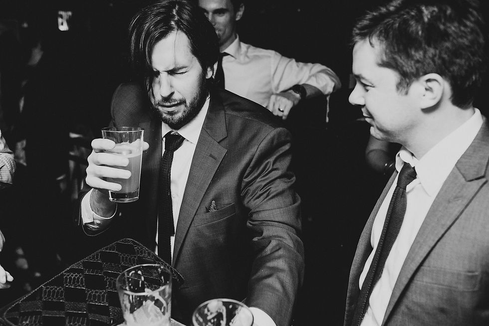 Groom talks with a seated guest while holding a drink