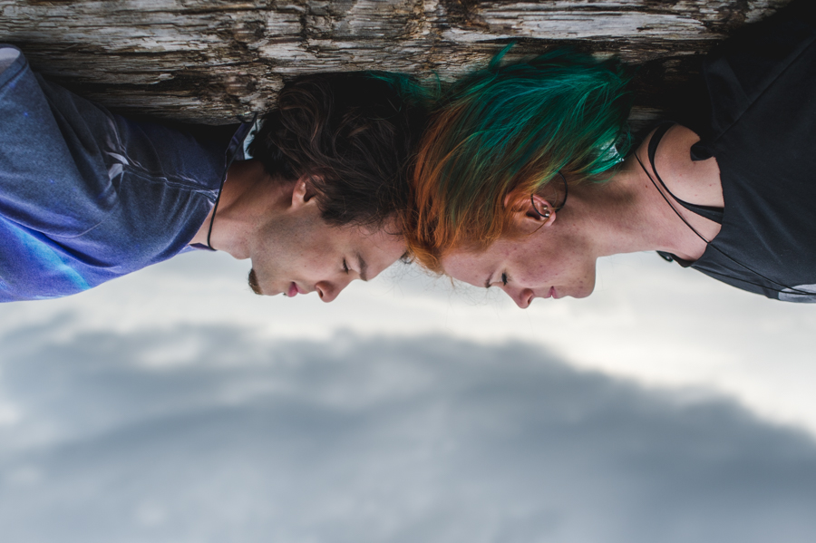 An inverted close view of two people lying with their heads near each other beneath a log.