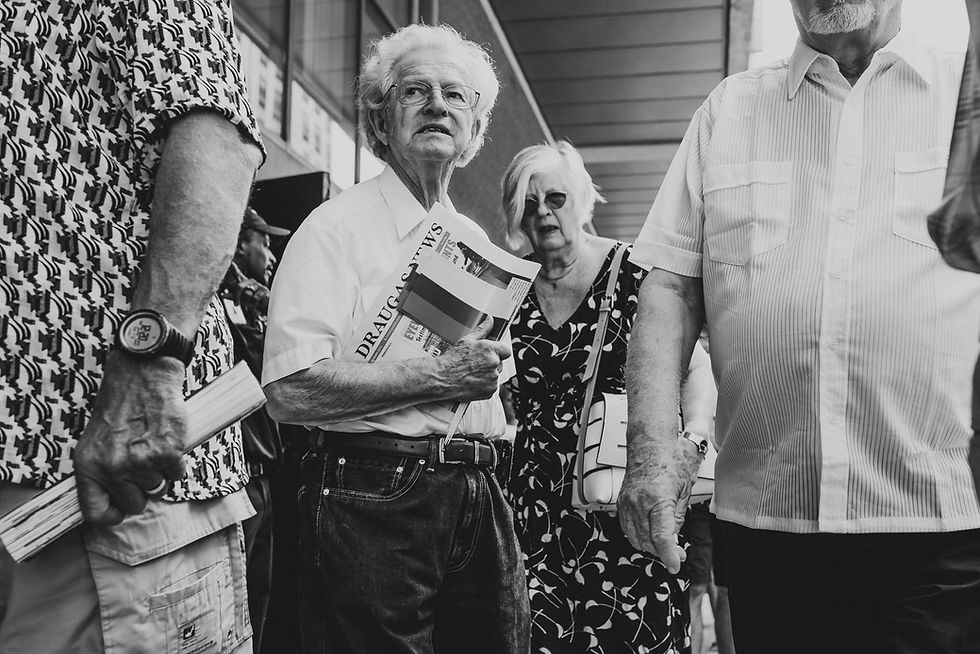 Black-and-white photograph of people standing together, including a man holding a folded newspaper.